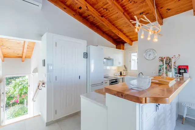 De keuken met witte kasten, een dikke houten bar en een houten balkenplafond.