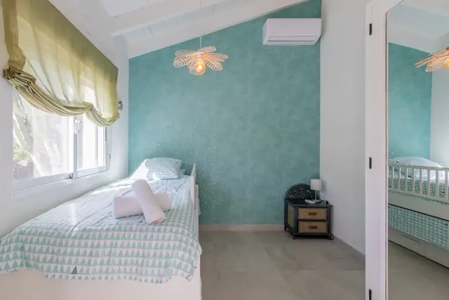 Een slaapkamer met een zeegroene wand, airconditioning en een rieten hanglamp.