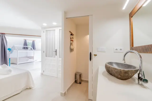 Een tweepersoonsbed, en door de openstaande deur een kinderbed in de vorm van een huisje; rechts op de voorgrond een wasbak van steen.